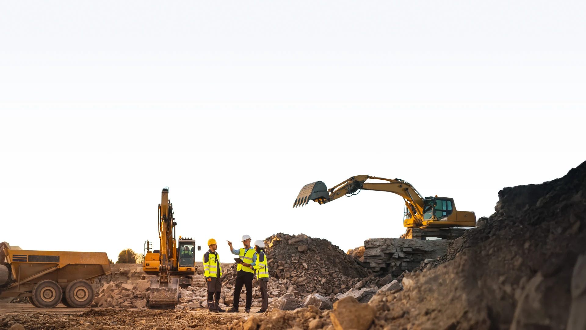 Construction crew reviewing plans with excavators and a haul truck at a worksite