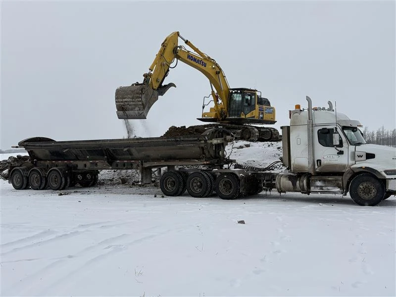 Excavator loading a side-dump truck for soil hauling