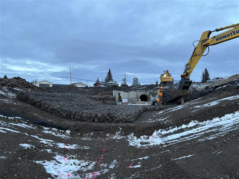 Excavator working beside a culvert and drainage channel in winter