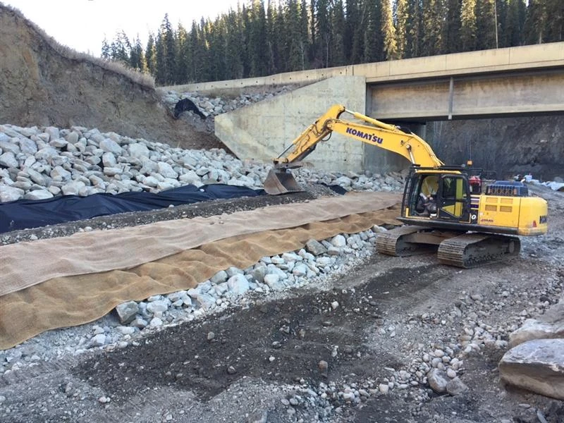 Excavator placing erosion protection beside a bridge and waterway