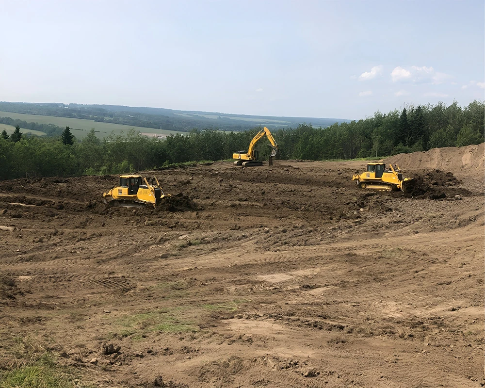 Excavators and a dozer restoring disturbed ground beside a forest